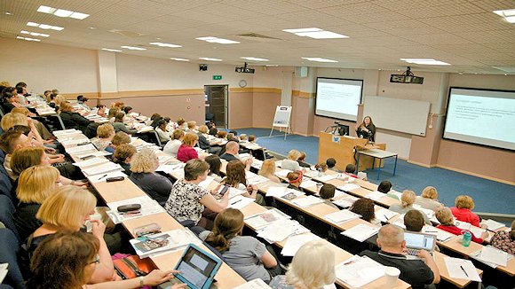 Attendees in tiered lecture theatre, and a lady speaking at the front