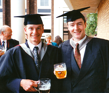Two male graduates pose in their finery with beers